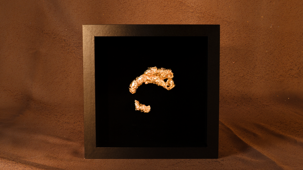 Gold-colored object resembling a stylized letter 'C' on a black background within a gold frame.