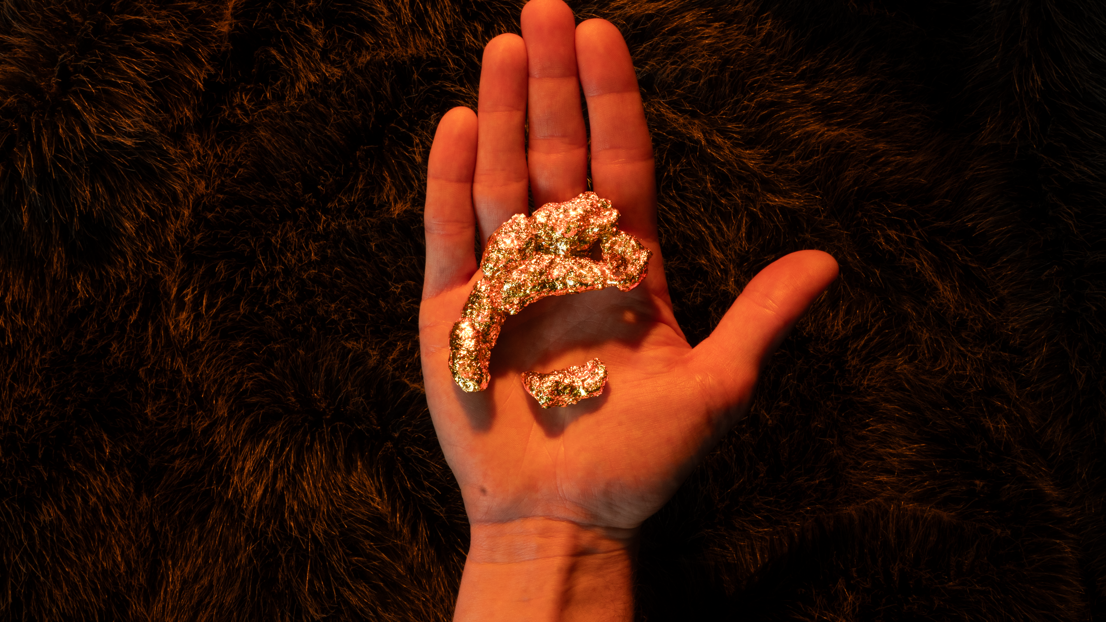 Hand holding a small pile of gold nuggets against a dark background